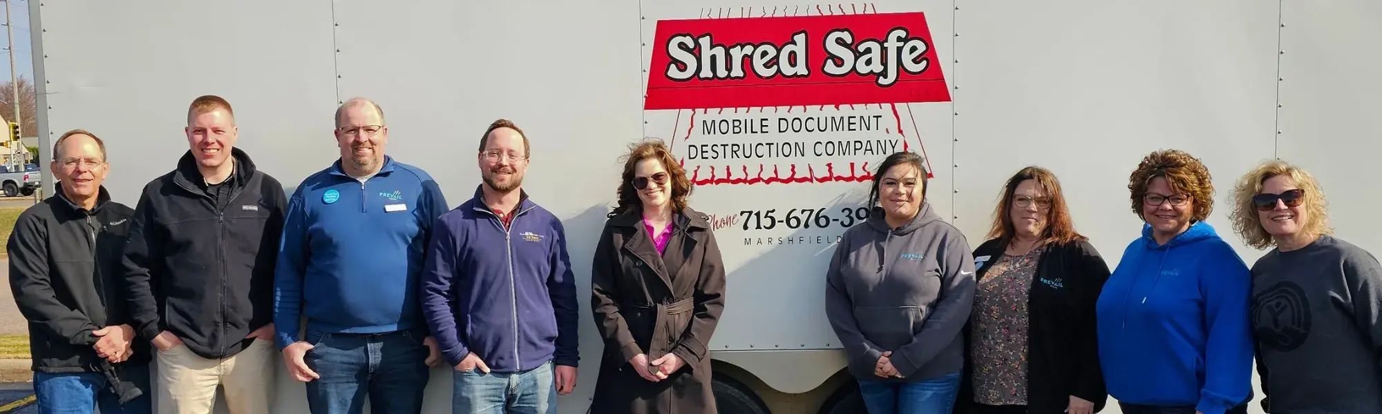 9 women and men smiling in front of the Shred Safe box truck